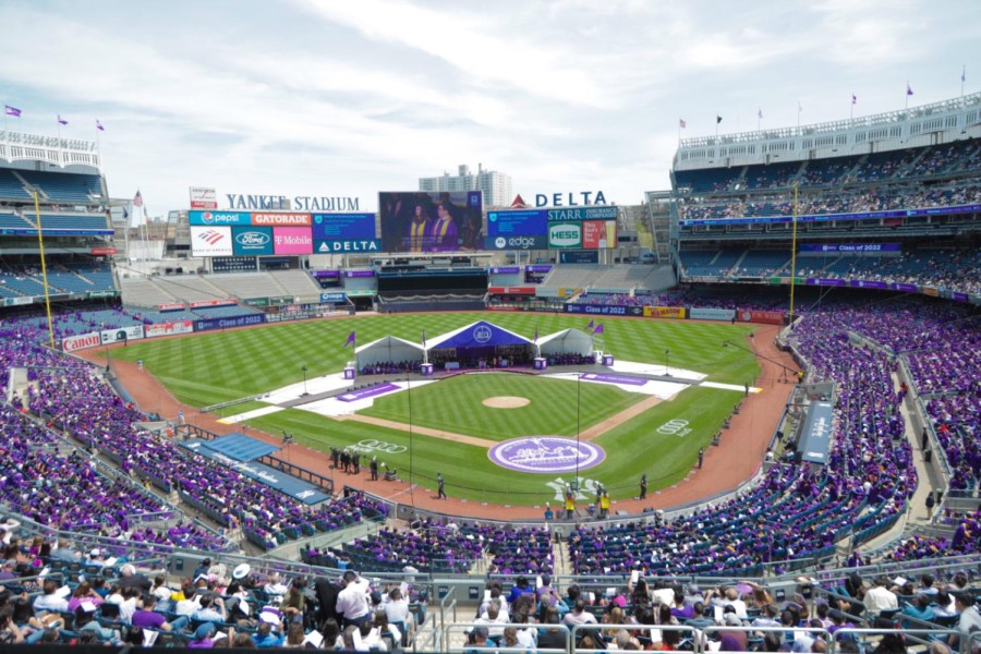 A photo of the inside of Yankee Stadium during N.Y.U.’s Class of 2022 graduation ceremony. The stadium is full of N.Y.U. students wearing purple robes. There are white tents set up on the field.