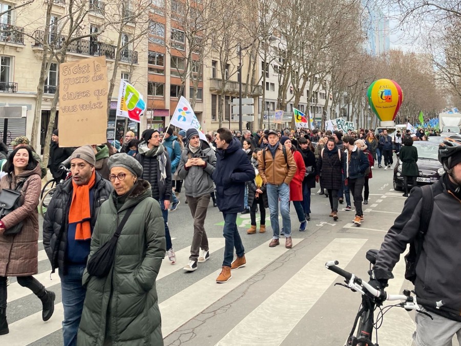 Photo of a street filled with people walking holding signs, and a yellow, green and red balloon floating in the back with the text “F.S.U.” printed on it.