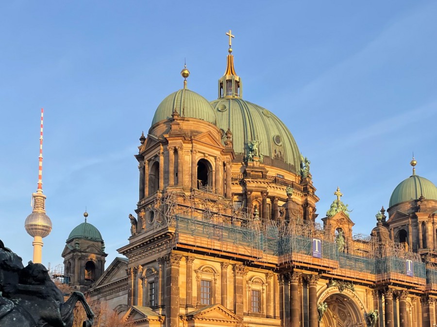 The Berlin Cathedral exterior lit up with sunshine. The television tower Berliner Fernsehturm is in the background.