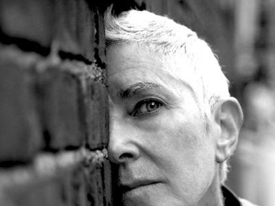 A black and white photo of visual artist Beth B. leaning against a wall.