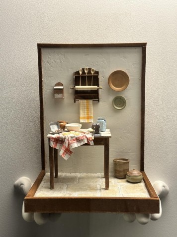 An exhibit of a miniaturize kitchen. There are utensils hanging on the wall and a table with ingredients for pasta on it.