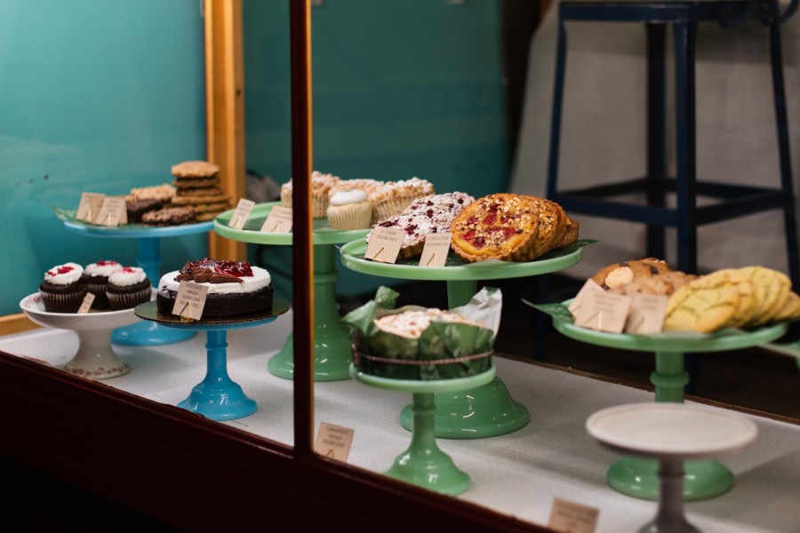 Two rows of different pastries and desserts placed on green, blue and white display plates inside a display window.