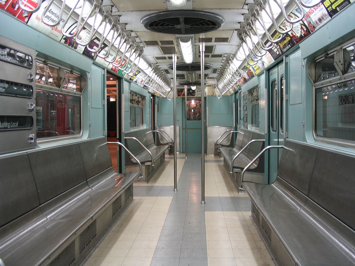 The interior of a subway car with light blue walls and gray bench chairs.
