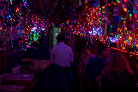 The interior of a dark restaurant with many colorful string lights hanging from the ceiling. There are customers in the restaurant and a waiter.
