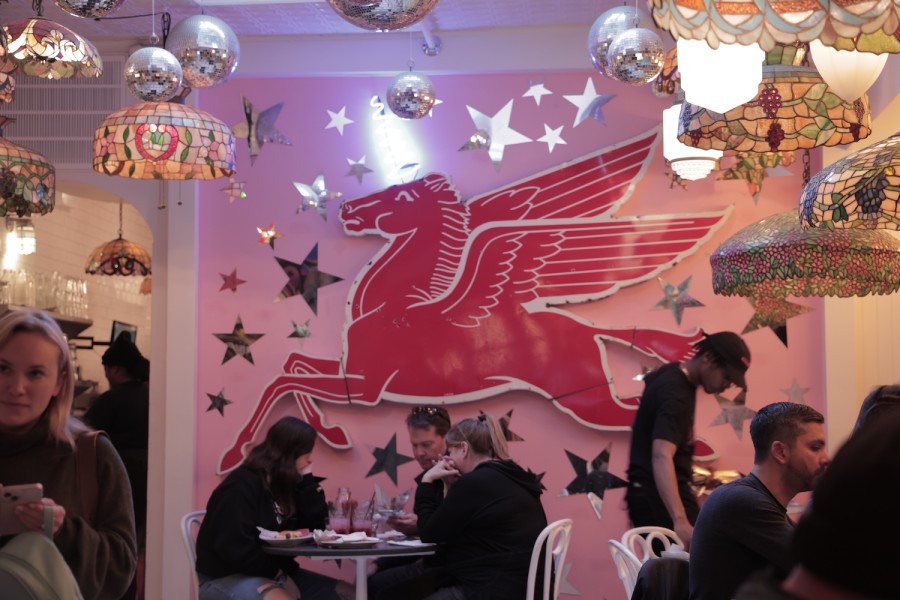 The interior of a restaurant with a pink pegasus on the wall and lamps of different shapes. There are customers sitting in the restaurant.