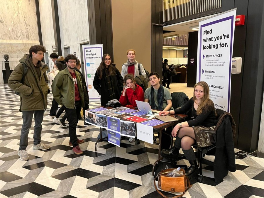 Seven people sit and stand around a table in the lobby of the New York University Bobst Library.  The Turkish flag is printed on the table.