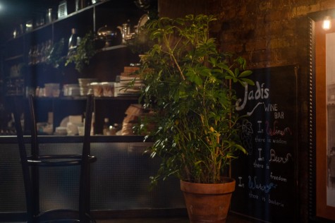 The interior of a restaurant with a plant and an upside-down barstool. Next to the plant is a blackboard with the text “Jadis” written with chalk on it.