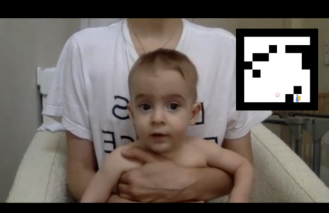A person wearing a white T-shirt and holding a baby. There is a black-and-white geometric logo superimposed in the top right corner of the frame.