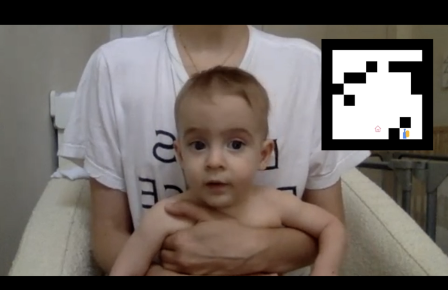 A+person+wearing+a+white+T-shirt+and+holding+a+baby.+There+is+a+black-and-white+geometric+logo+superimposed+in+the+top+right+corner+of+the+frame.