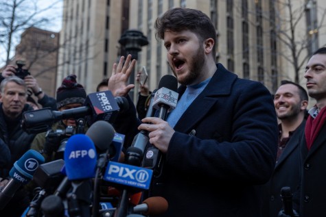 A man wearing a navy blue jacket standing in a large crowd of people speaking into an RSBN microphone.