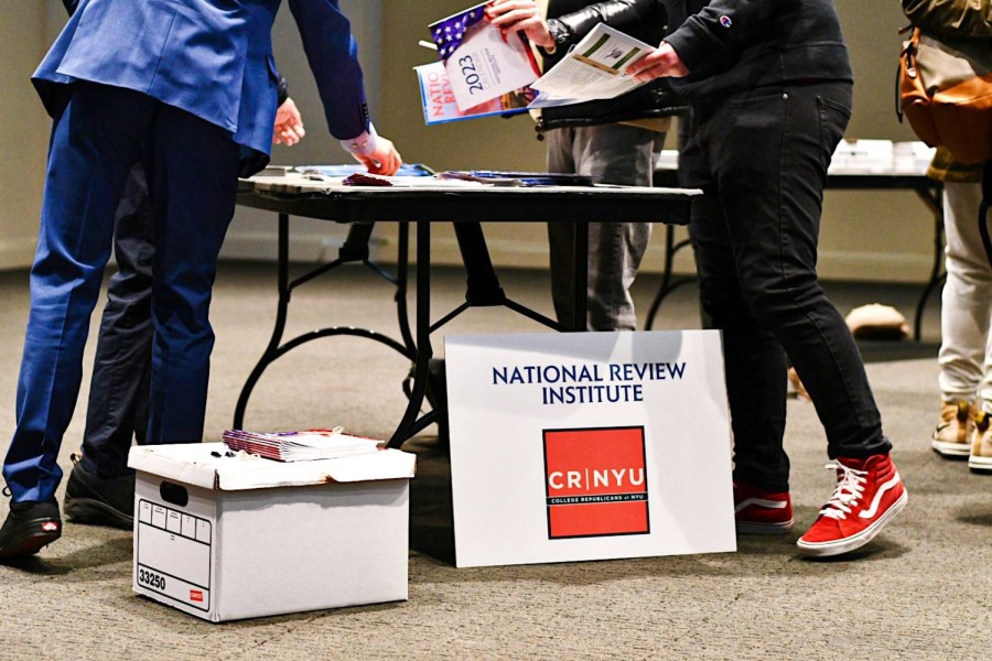 A group of people standing around a table with a sign propped up against it. The sign reads “National Review Institute” and “College Republicans at N.Y.U.”