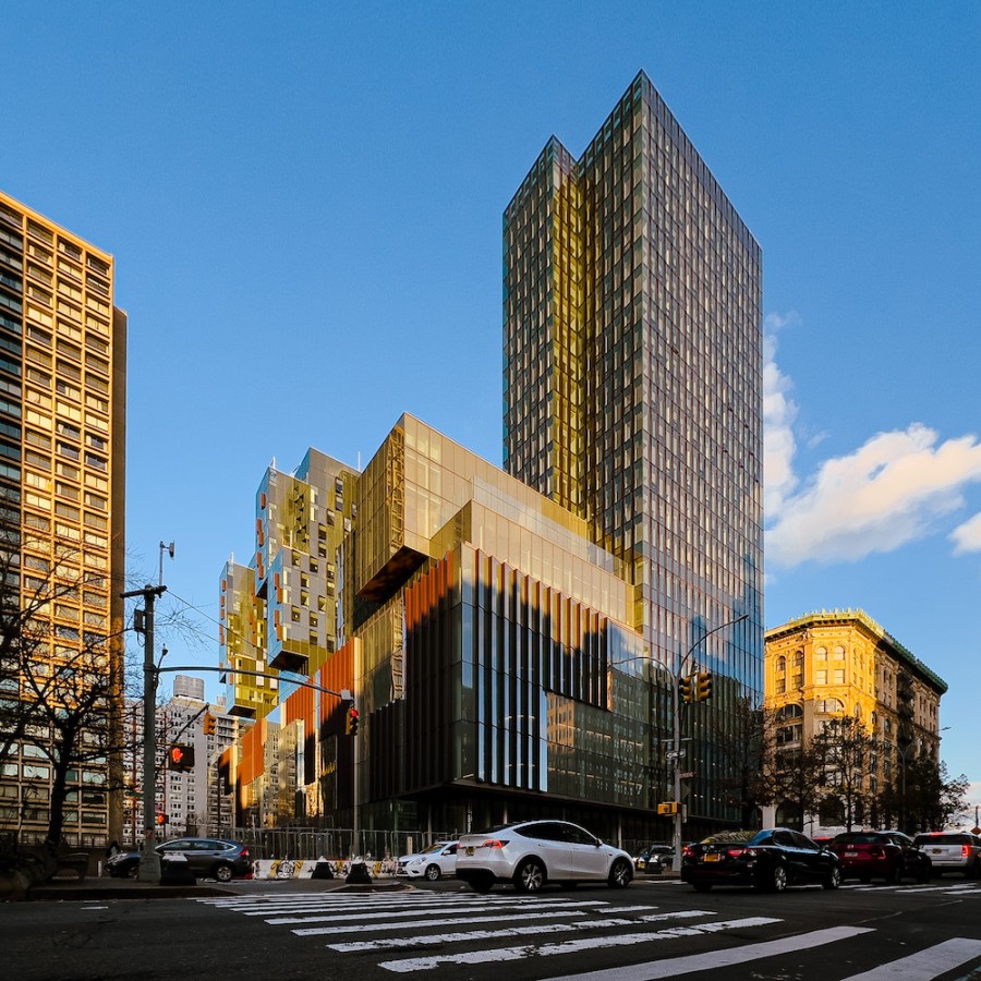 A tall building complex with a glass exterior and traffic passing in front.