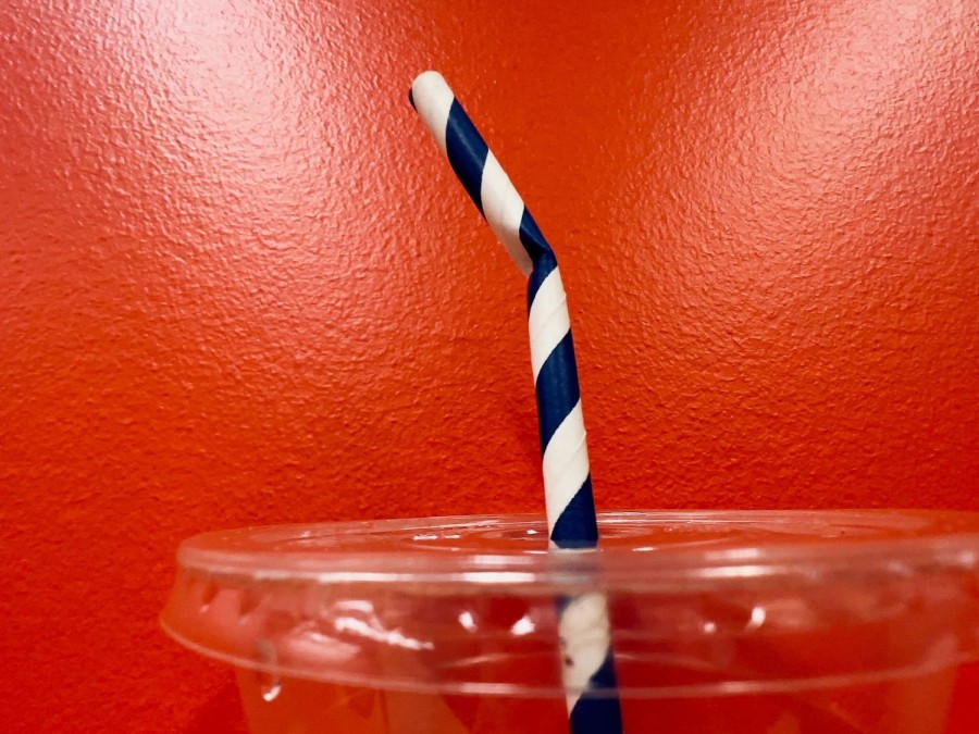 A paper straw with blue stripes in a plastic cup against a red wall.