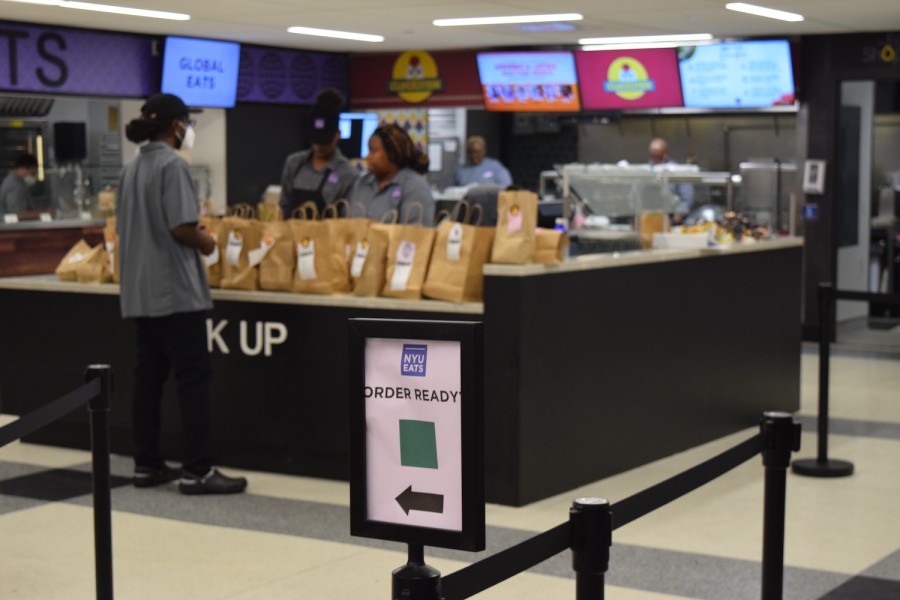 The entrance to N.Y.U’s Upstein dining hall with a sign that reads “Order Ready.” There is a pick-up counter in the background with many brown paper bags waiting to be collected.