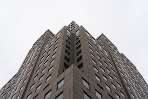 The 80s/90s architecture of 1 Metrotech. One Metrotech is photographed with the angle being adjacent to the building at ground level. There is a dark facade and many windows to compliment the angular design of the building.
