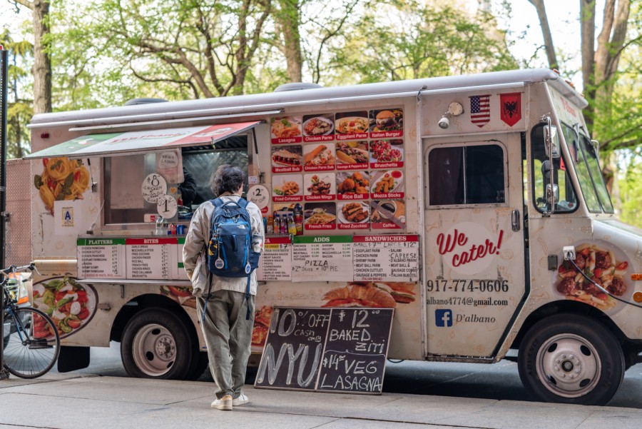The exterior of a white food truck covered in menu items and signs that read “ten percent off, N.Y.U. Cash only. Twelve dollar ziti. Fourteen dollar veg lasagna.”