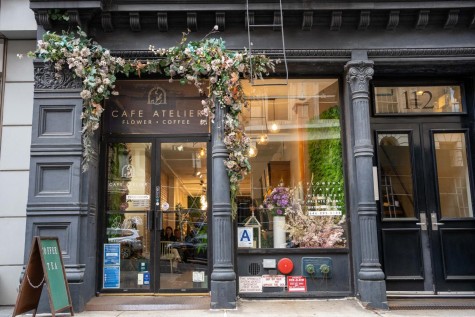 The storefront of a restaurant called “Cafe Atelier” with flowers placed inside the windows and above the entrance.