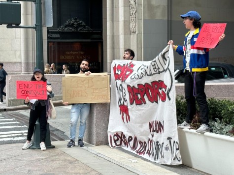 A group of people standing on a street corner holding various signs that read, “END THE CONTRACT!”, “LEXIS SURVEILS ICE DEPORTS”, “NO TECH FOR ICE!!”