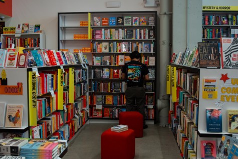 An interior space surrounded on all sides by bookshelves. In the middle are two red chairs. In the background, a person wearing a black shirt stands in front of a bookshelf.