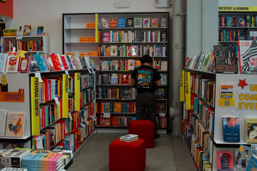 An interior space surrounded on all sides by bookshelves. In the middle are two red chairs. In the background, a person wearing a black shirt stands in front of a bookshelf.