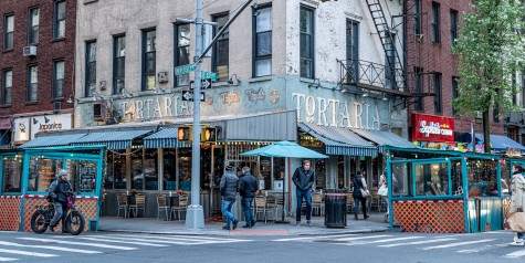 Light blue exterior of a restaurant with a white sign that reads “Tortaria.” It has an outdoor seating area.
