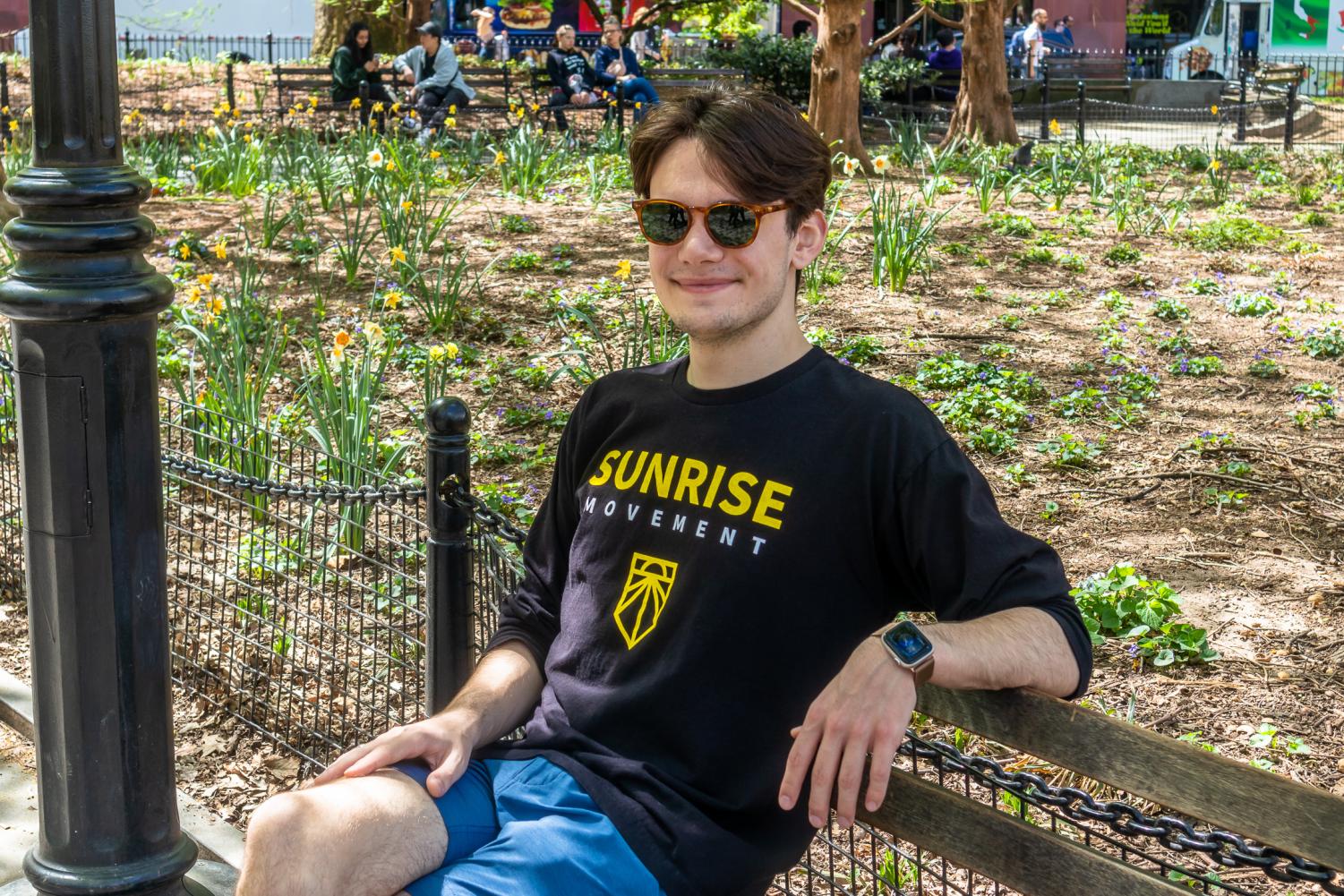 Dylan Wahbe, the hub coordinator for Sunrise NYU, sitting on a bench with a “Sunrise Movement” tee shirt
