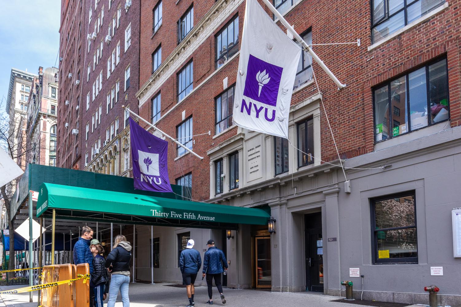 The exterior of NYU’s Rubin Hall with passersby and NYU flags.