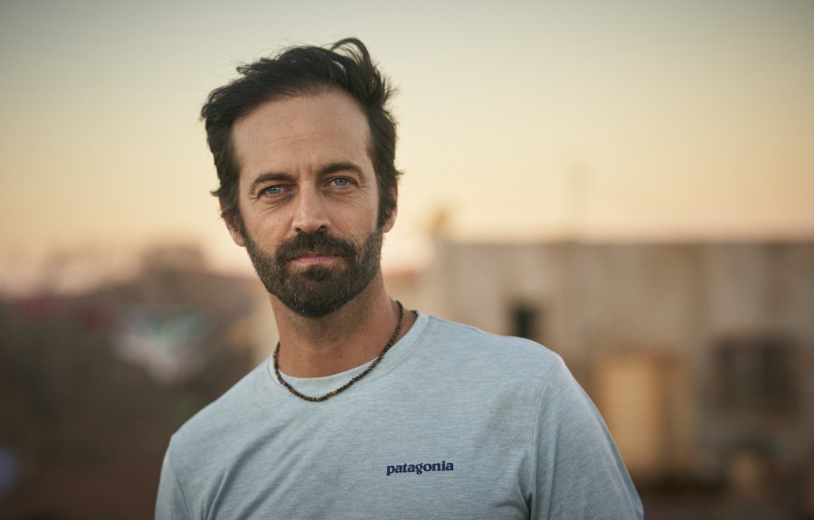 A photograph of Director Benjamin Millepied in a gray t-shirt, against a blurred background of various buildings against the sky.