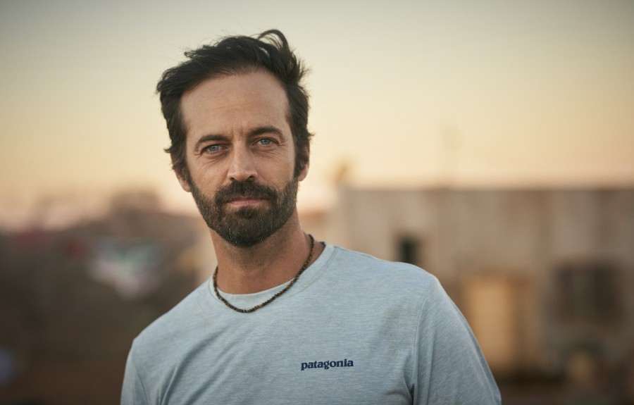 A+photograph+of+Director+Benjamin+Millepied+in+a+gray+t-shirt%2C+against+a+blurred+background+of+various+buildings+against+the+sky.