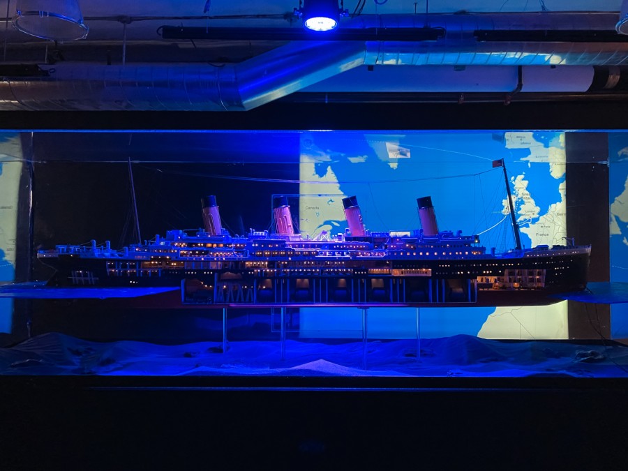 A replicate model of the cruise ship Titanic showcasing its internal structures. The model is placed in a transparent display case lit up by dim, blue lighting.