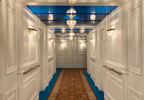 A replicated first-class hallway of the cruise ship Titanic with white walls, and blue-red carpeting.
