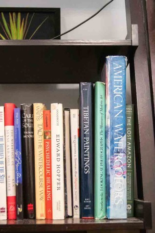 Several books sit in a bookshelf, including one titled “American Watercolors,” one titled “Tibetan Paintings,” and another titled “Psychedelic Healing.”