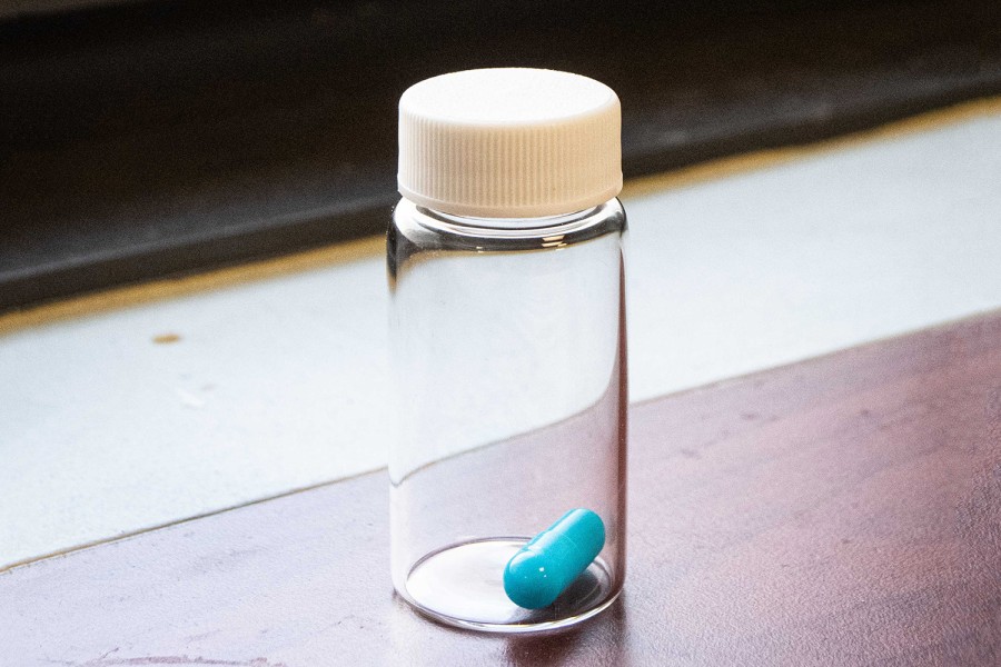 A blue psilocybin capsule inside a glass can placed on a windowsill.