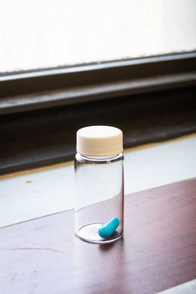 A single blue psilocybin capsule inside a glass bottle that is placed on a windowsill.