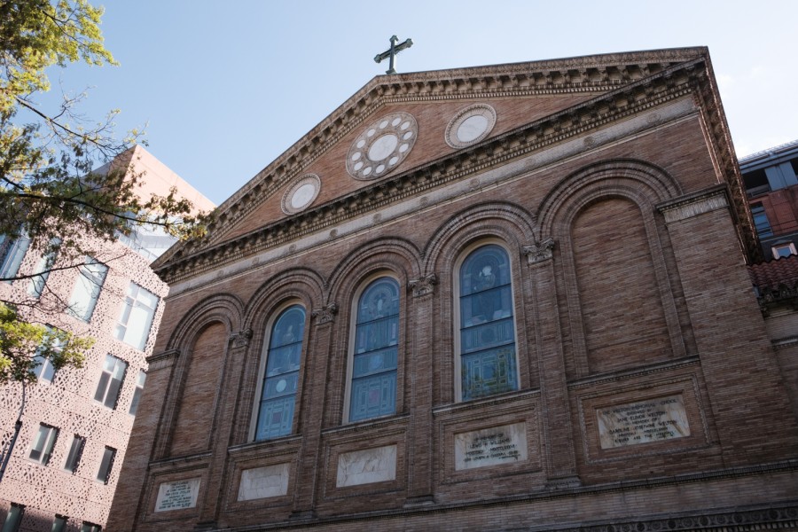 The façade of Judson Memorial Church, which has columns made of red bricks, stained windows and a cross at the top.