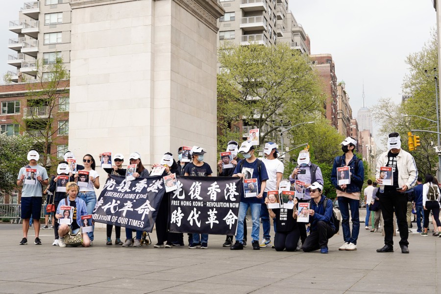 Protesters wearing white masks standing under the Washington Square Arch, holding posters with the names and photos of Hong Kong political prisoners, and two banners, one of which says “Liberate Hong Kong, Revolution of Our Times” in both Chinese and English.