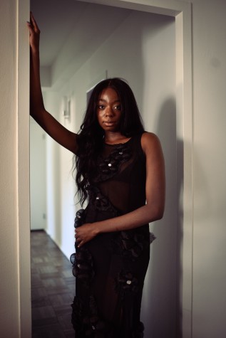 Samantha Harper, founder of Harper Collective, stands in the hallway of her apartment. She is wearing the superbloom dress in noir.