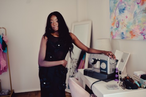 Samantha Harper, founder of Harper Collective, stands in her room by her sewing machine. She is wearing the superbloom dress in noir.