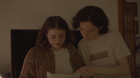 Two people read from a sheet of paper together in a dimly lit room.