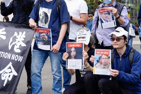 Protesters wearing white masks holding posters with the names and photos of Hong Kong political prisoners.
