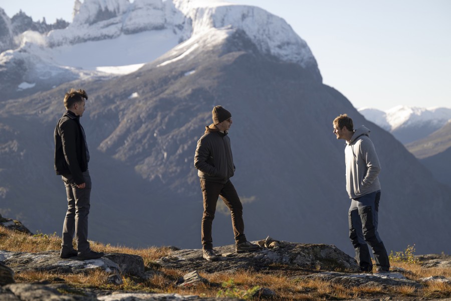 Kieran Culkin, Jeremy Strong and Alexander Skarsgård stand on grass and rocks in front of snow-capped mountains.
