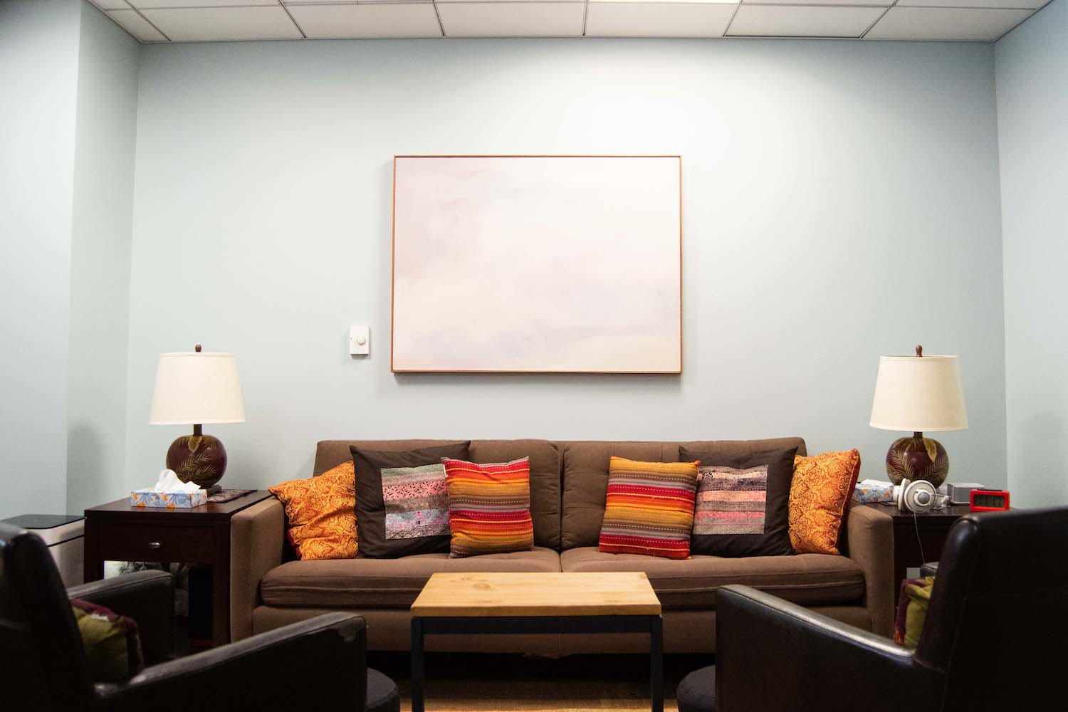 A brown couch with orange pillows in a room with blue walls.