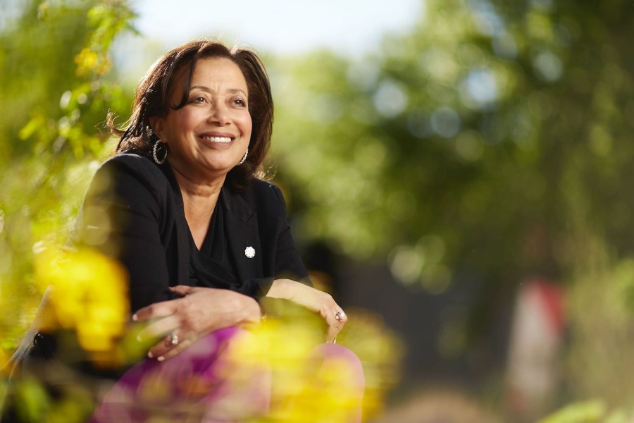 Angela Amar dressed in black formal attire, surrounded by out-of-focus plants.