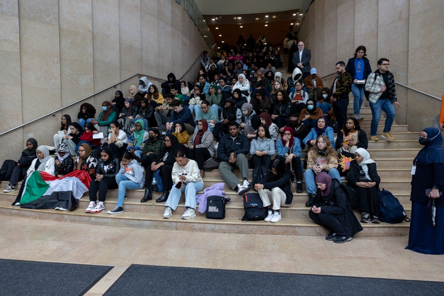 A big crowd of people sit on ascending tan marble steps, many of them with their heads facing down and their eyes closed.