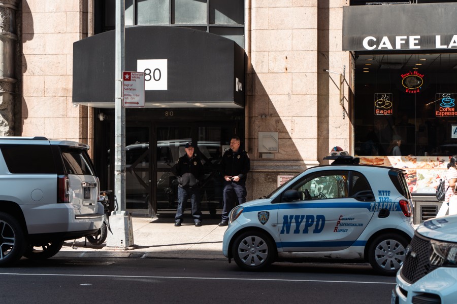 Two N.Y.U. security officers standing outside the entrance to N.Y.U.’s Lafayette residence hall with a small police car parked on the street