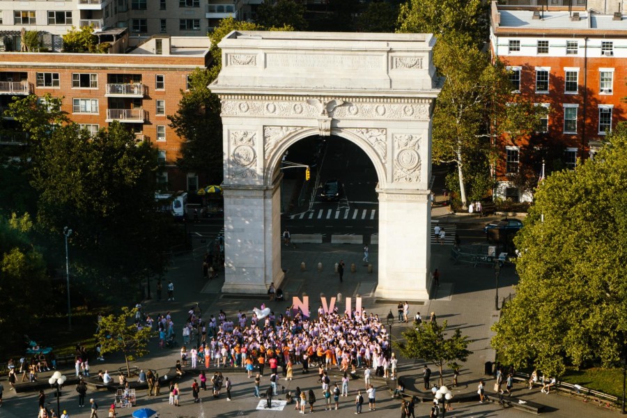 An aerial view of the Washington Square Arch with a crowd of N.Y.U. students wearing purple outfits in front.