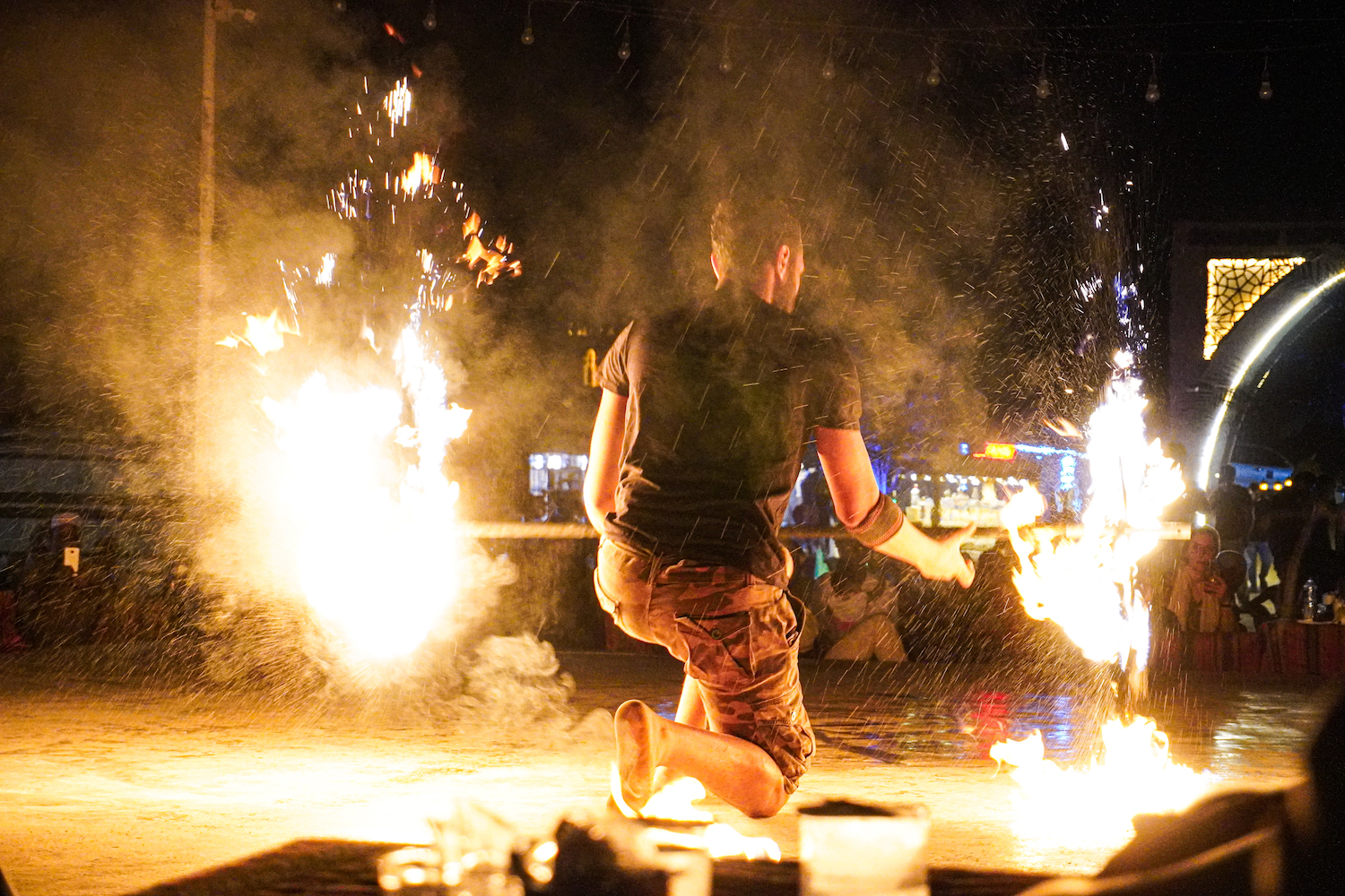 A man in a black shirt and cargo shorts standing on a stage holds a rod with fire coming out of both sides.