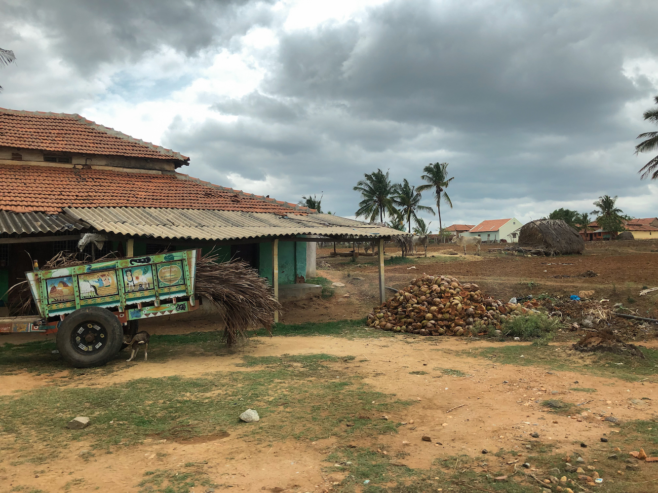 A village house in Channapatna, Karnataka, India, with coconut shells and a colorful wheelbarrow in front.