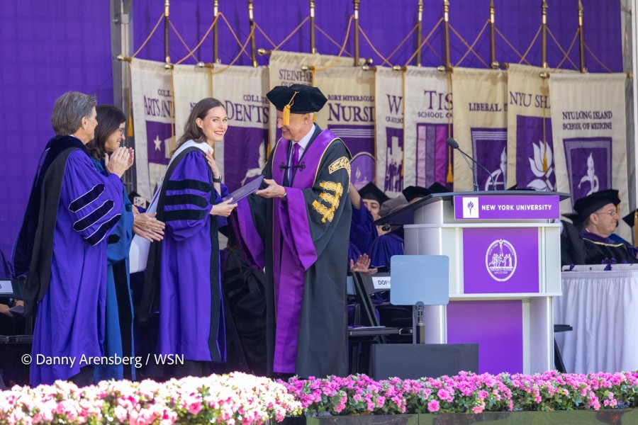 Finnish+Prime+Minister+Sanna+Marin+receives+an+honorary+diploma+from+N.Y.U.+President+Andrew+Hamilton.+White+banners+displaying+N.Y.U.+school+names+and+logos+in+purple+are+draped+behind+Marin+and+Hamilton.