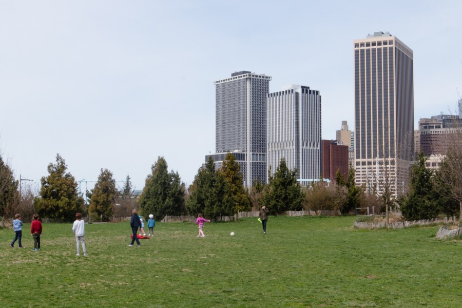 A view from the Brooklyn Bridge Park with people exercising on the grass and downtown Manhattan in the background.